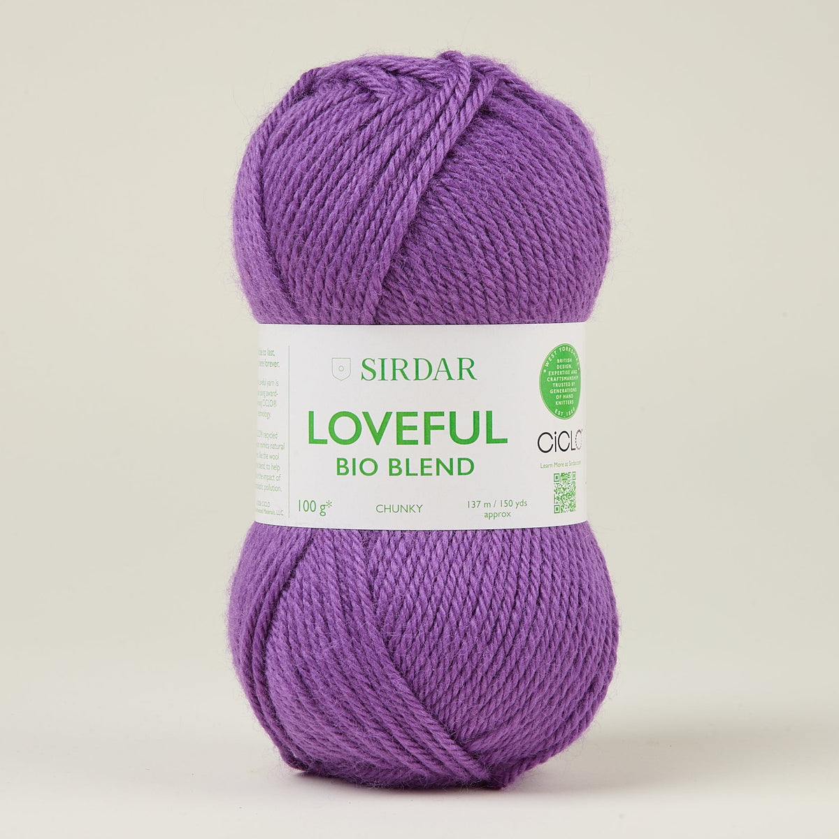 A single skein of Sirdar Loveful Bio Blend yarn in a medium purple shade, wrapped with its white paper label, set against a plain light beige background.